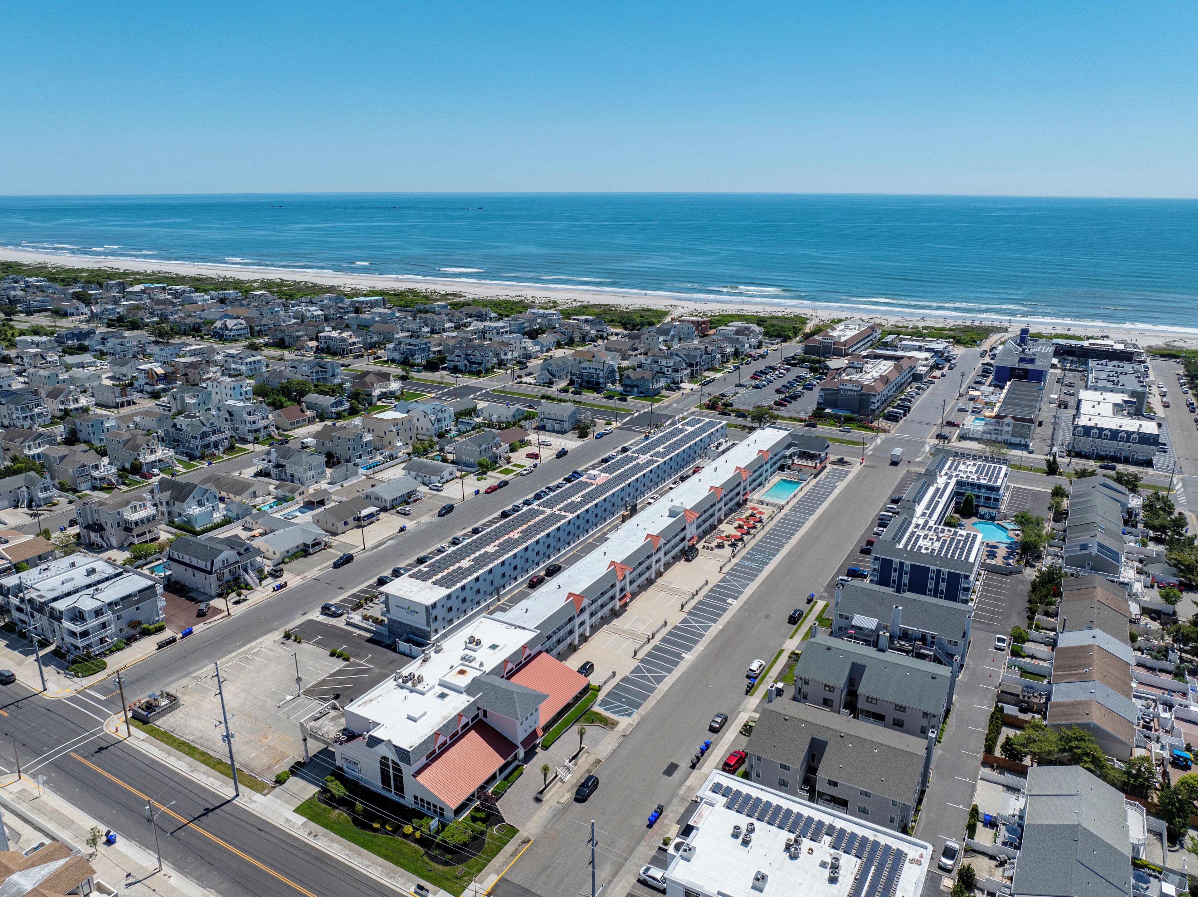 An aerial view of a coastal town with a marina, residential buildings, and a hotel with a swimming pool.