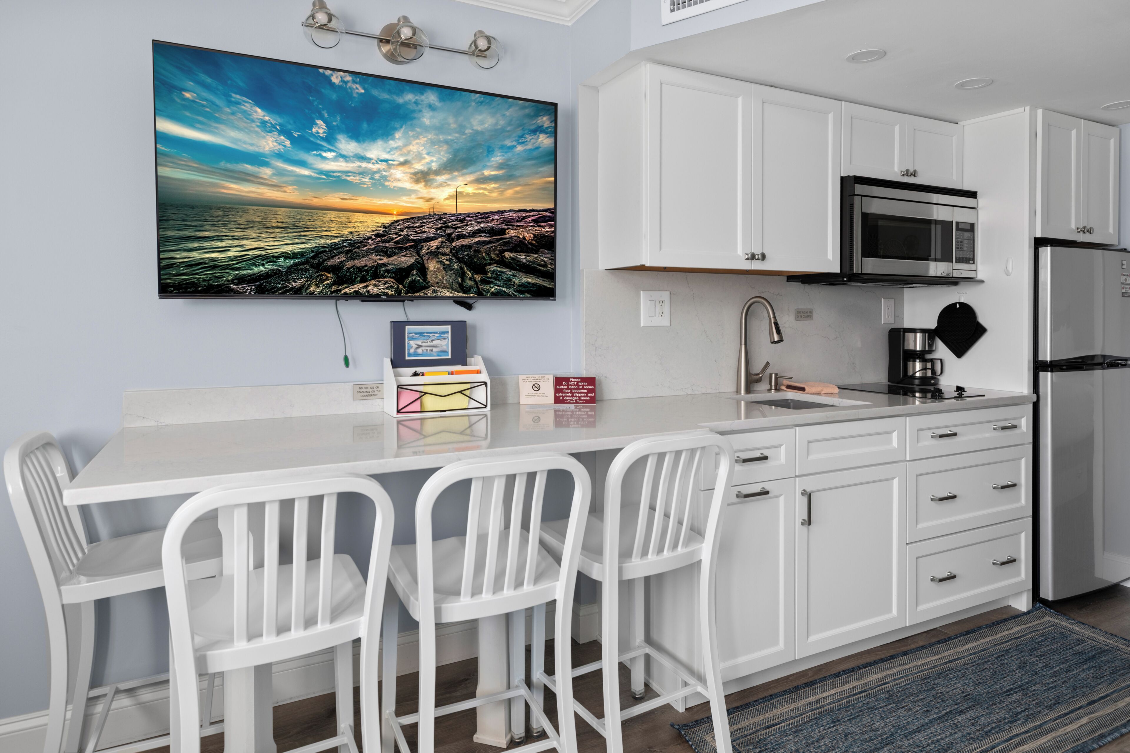 A modern kitchen with white cabinetry, a stainless steel refrigerator, a microwave, and a coffee maker.