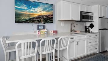A modern kitchen with white cabinetry, a stainless steel refrigerator, a microwave, and a coffee maker.