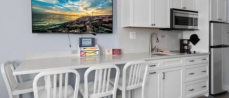 A modern kitchen with white cabinetry, a stainless steel refrigerator, a microwave, and a coffee maker.