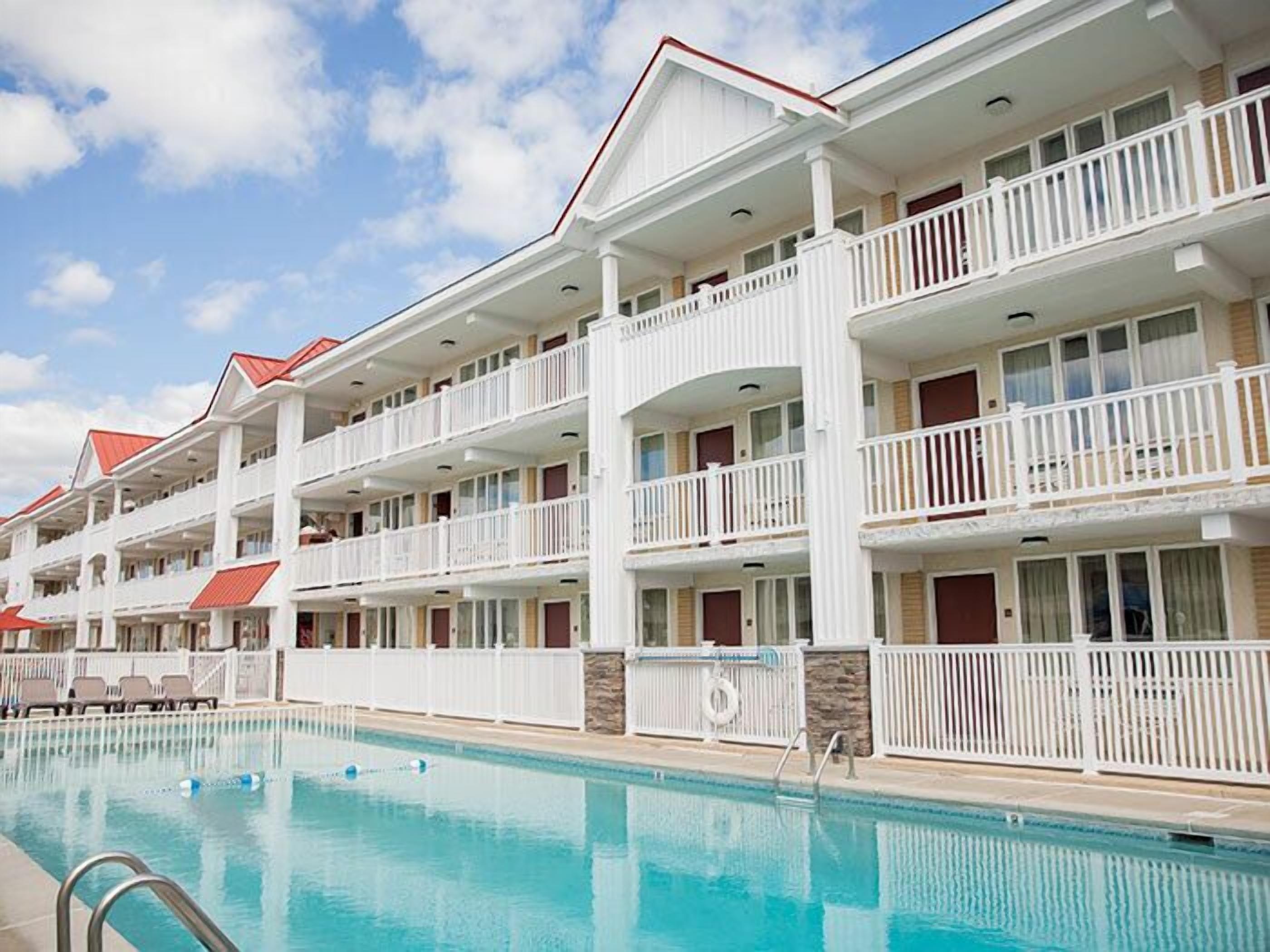 A multi-story hotel with balconies, a swimming pool, and a clear sky.