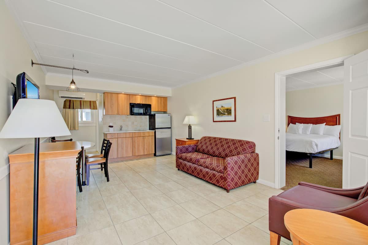 A compact hotel room with a kitchenette, a dining area, and a living area with a sofa and a bed.