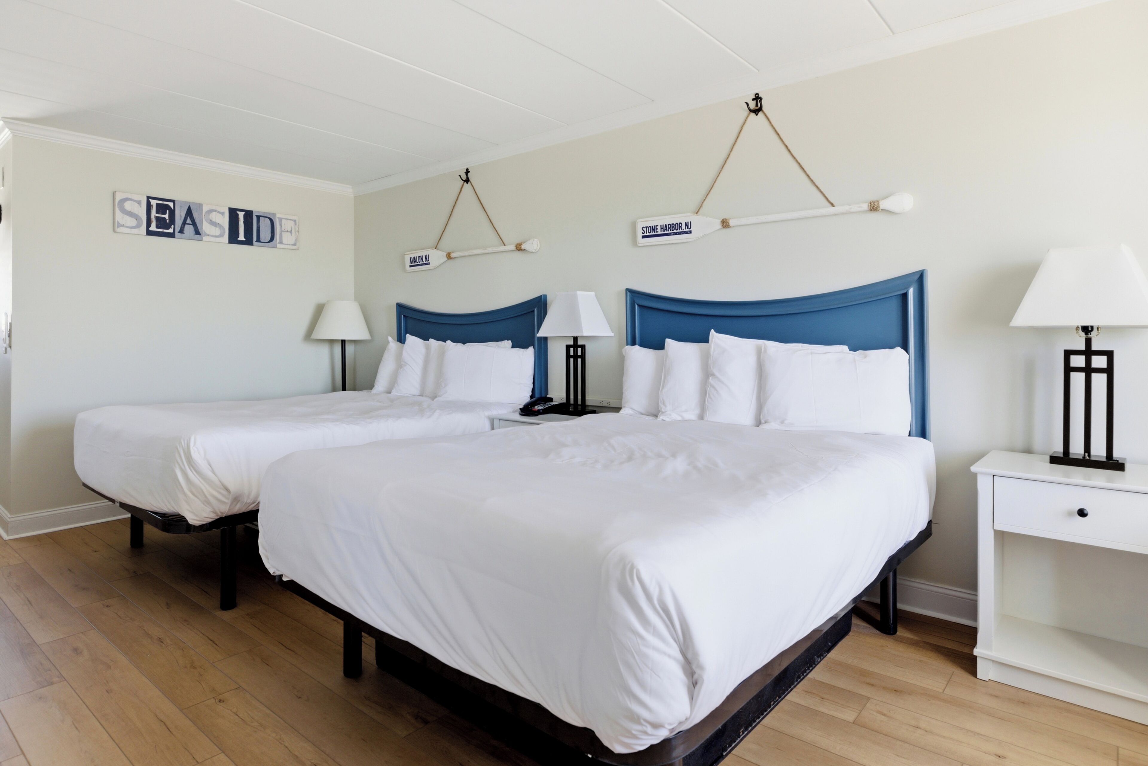 A hotel room with two beds, a white color scheme, and a sign indicating 'SEASIDE' and 'STONE HARBOR NJ'.