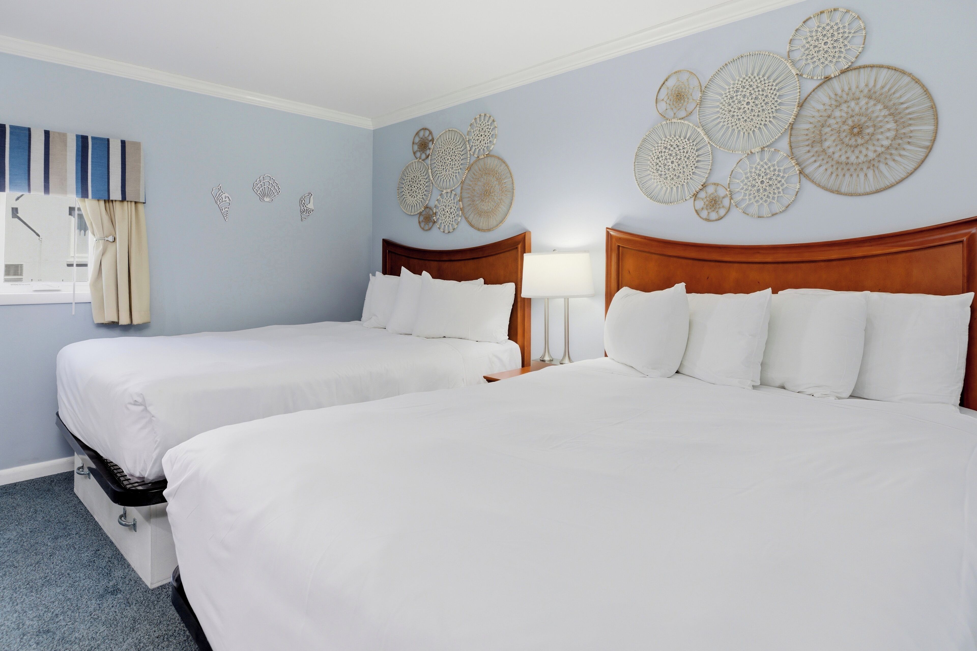 A hotel room with two beds, a window with curtains, and wall decor.