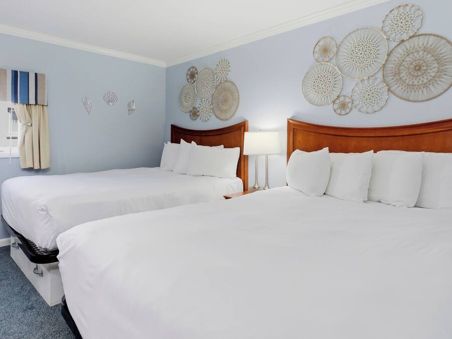 A hotel room with two beds, a window with curtains, and wall decor.