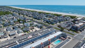 An aerial view of a coastal residential area with a hotel featuring a swimming pool and red-roofed buildings.