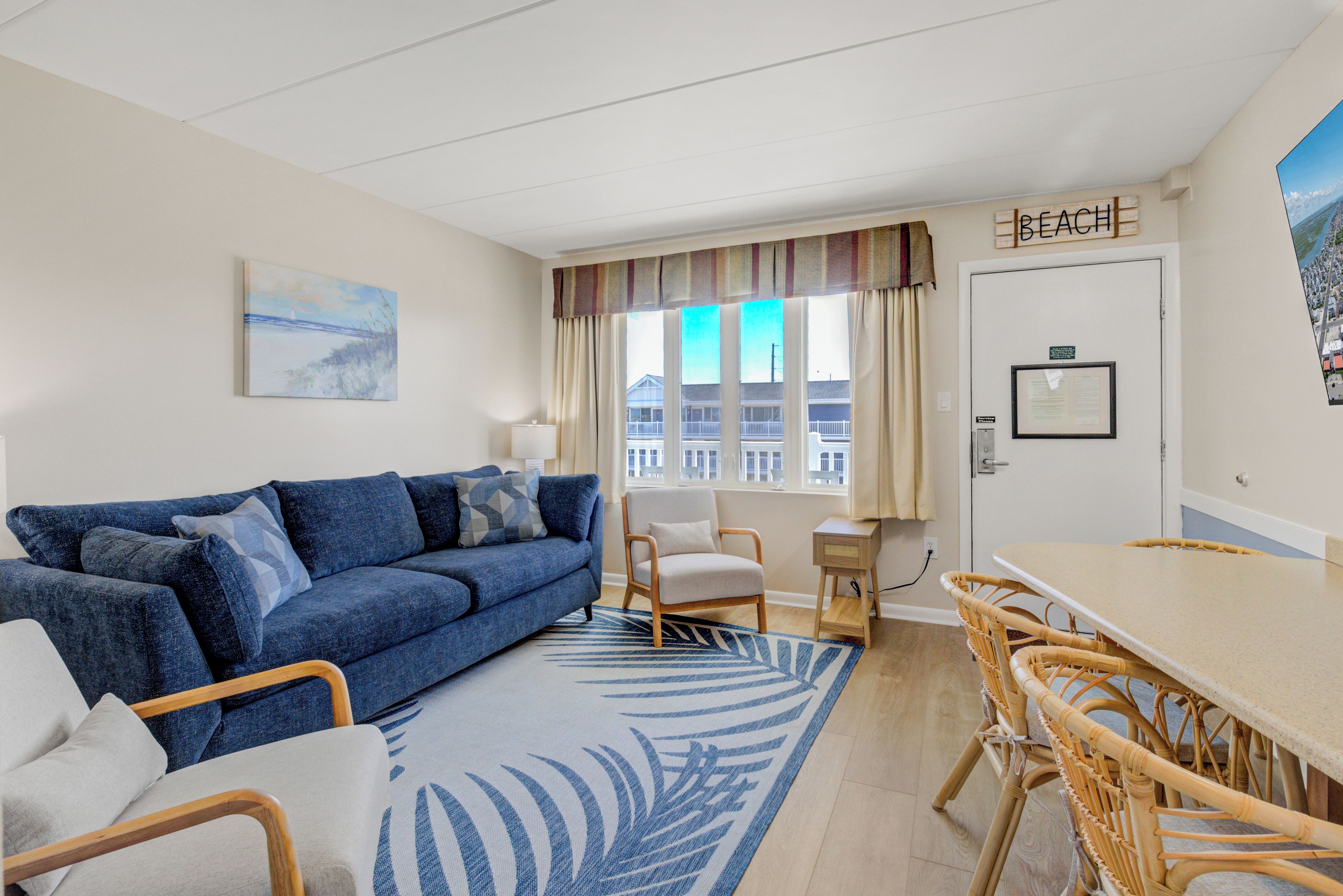 Une pièce avec un canapé bleu, une petite table, une chaise et une vue sur la plage par la fenêtre.