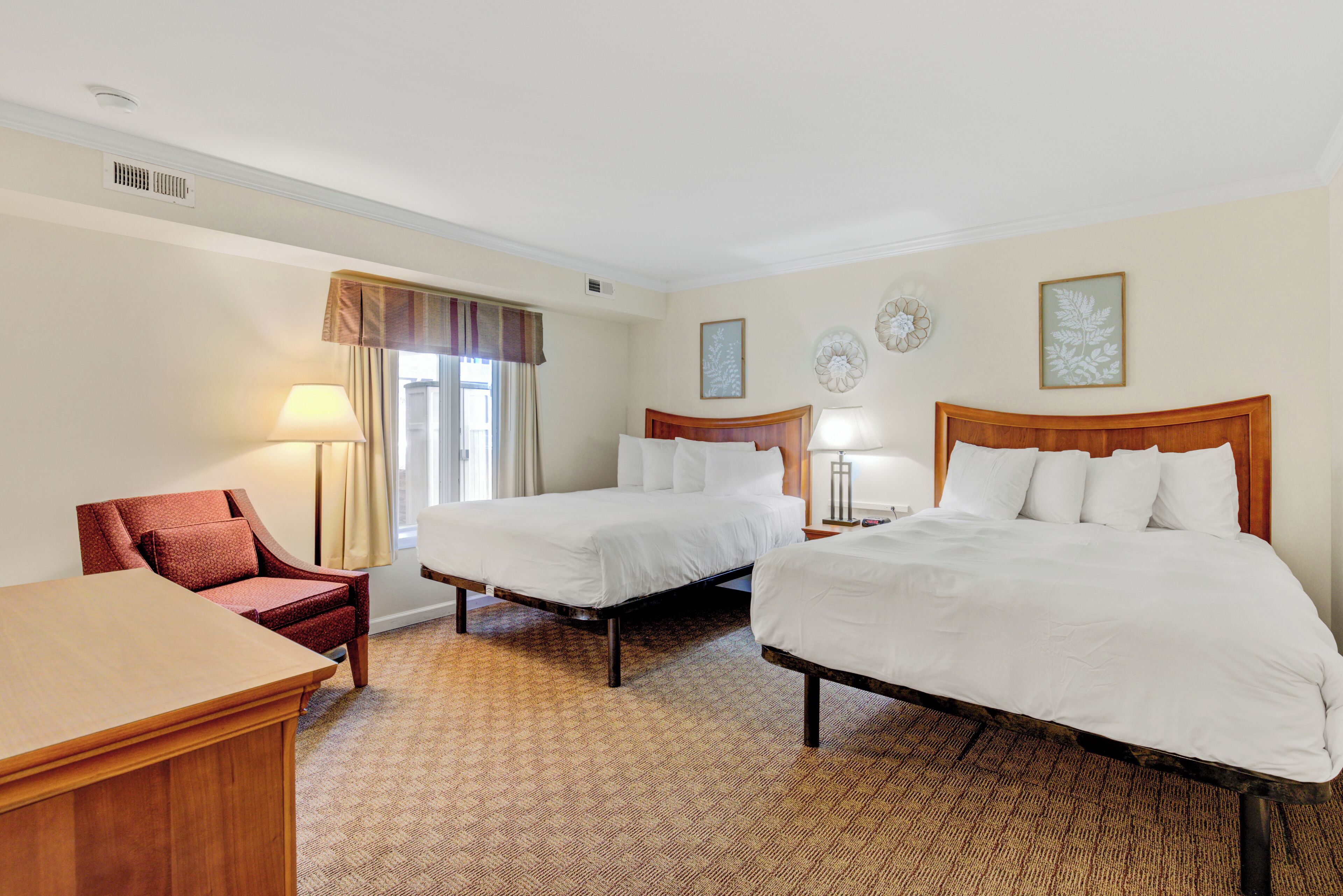 Una habitación de hotel con dos camas, un escritorio, una silla y un ventanal con cortinas.