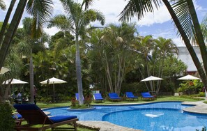 A pool area with lounge chairs and umbrellas, surrounded by palm trees.