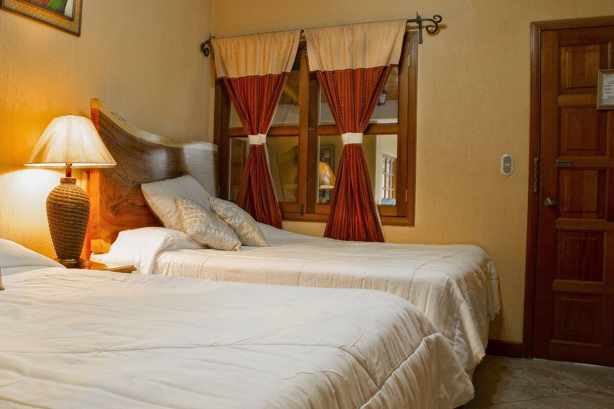 Une chambre d’hôtel avec deux lits, une tête de lit en bois, une lampe de chevet et une porte avec une plaque.