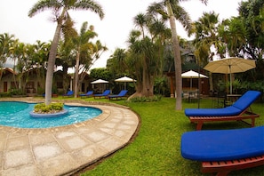 A pool area with lounge chairs and umbrellas, surrounded by palm trees and a well-maintained lawn.