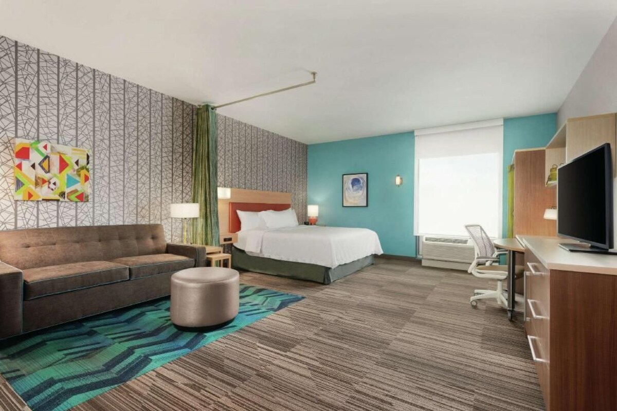 A hotel room with a bed, a sofa, a desk, a TV, and a patterned wall.