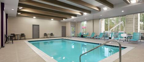 An indoor swimming pool with clear water, surrounded by lounge chairs and tables.