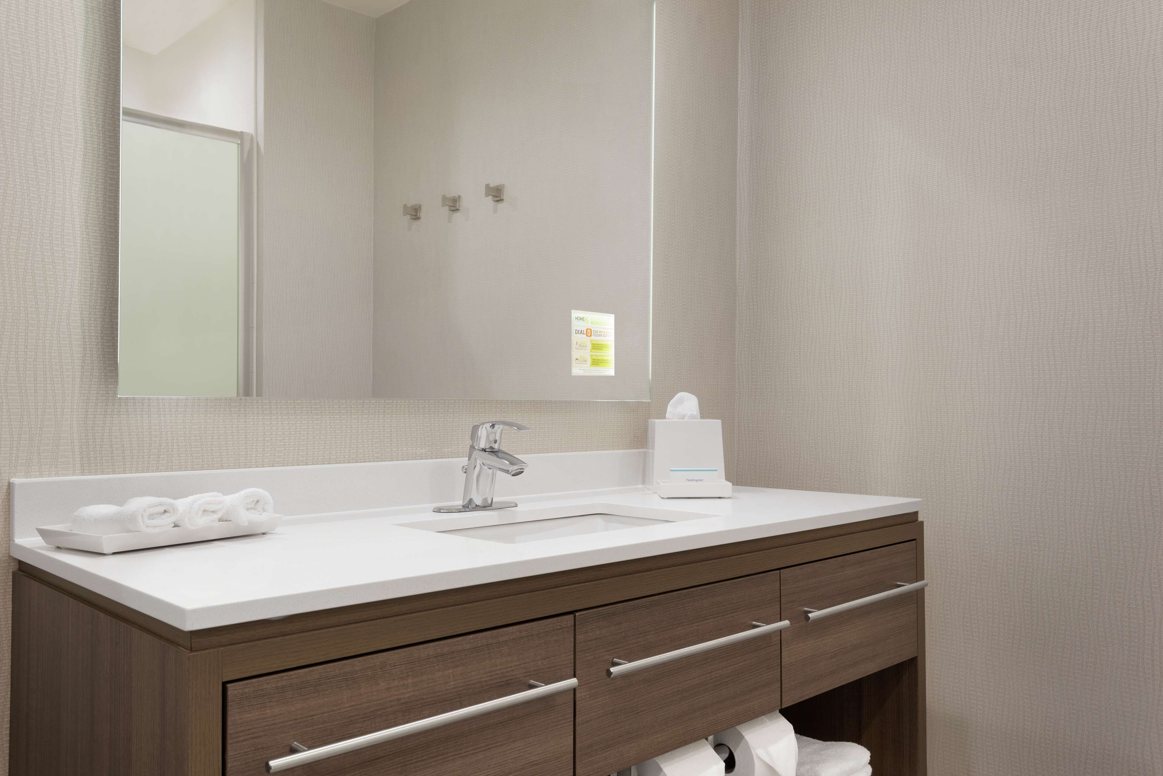 A modern bathroom with a white sink, a mirror, and wooden cabinetry.