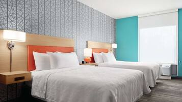 A hotel room with two beds, a patterned wallpaper, a teal accent wall, and a window with blinds.