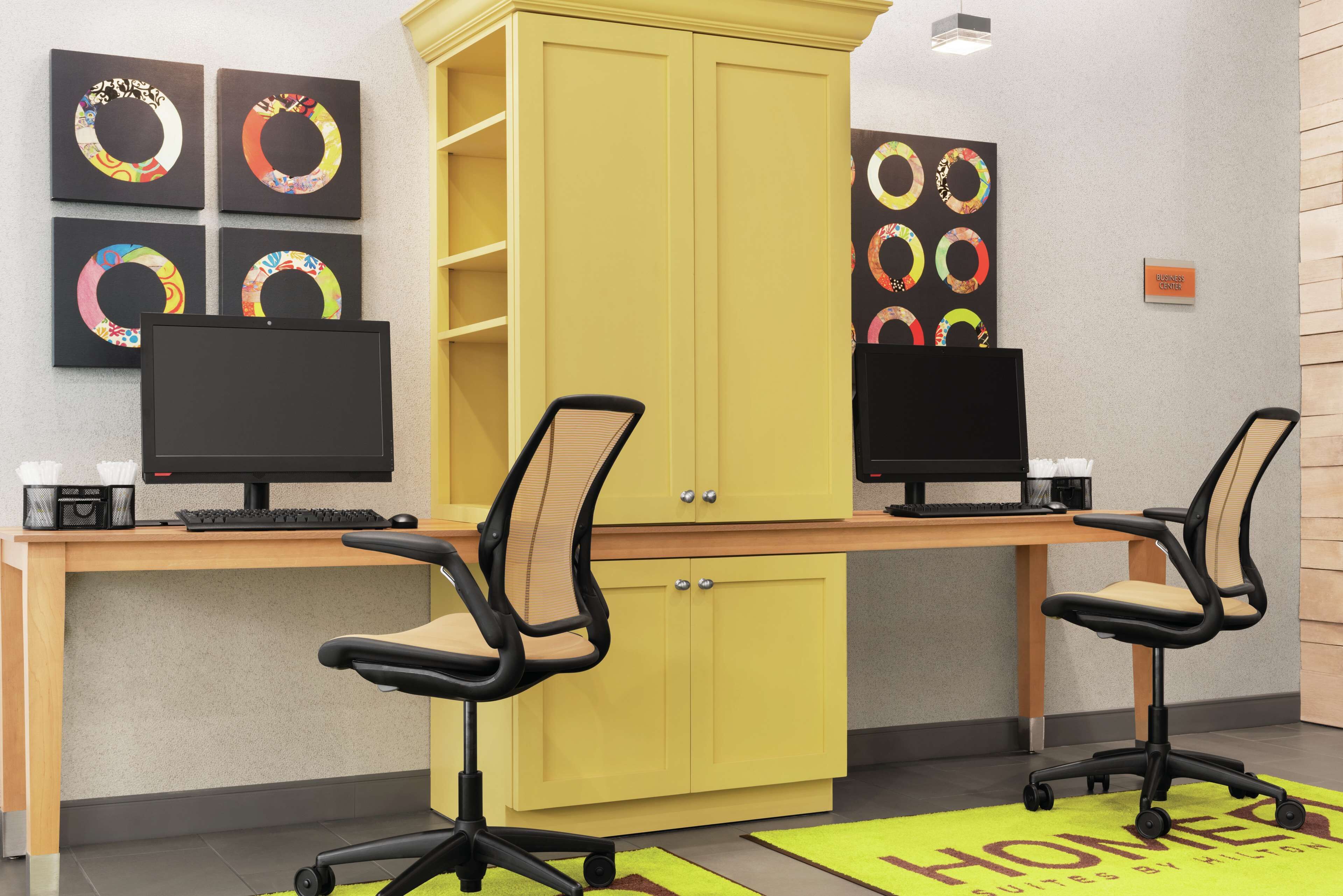 A workspace with two desks, each with a computer and office chair, and a yellow cabinet.