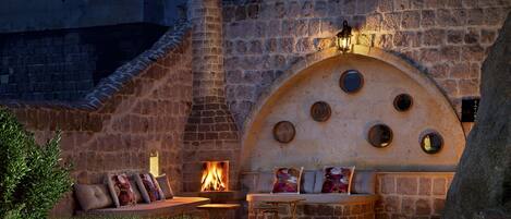 A stone building with a fire pit, seating area, and a stone wall with circular windows.