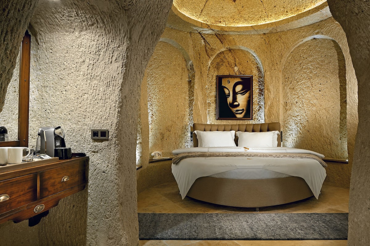 A bedroom with a stone wall, a bed, a painting, and a coffee machine.