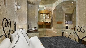 A stone-walled bedroom with a bed, a nightstand, and a bathroom visible through an archway. - Seraphim Cave Suites & Spa (Ürgüp)
