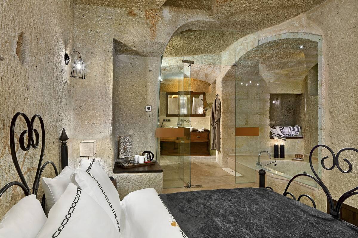 A stone-walled bedroom with a bed, a nightstand, and a bathroom visible through an archway.