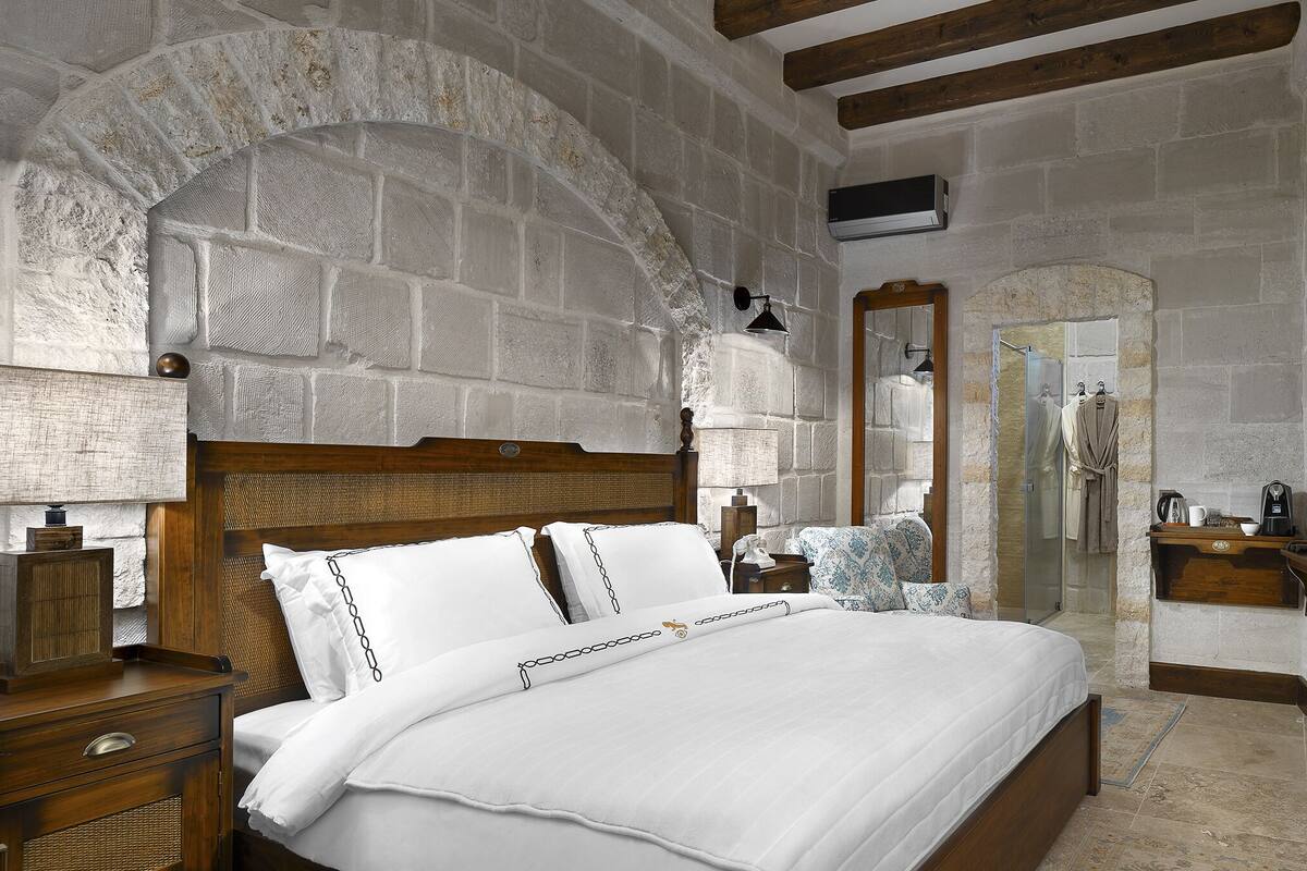 A bedroom with a stone wall, wooden bed frame, bedside tables, a mirror, and a dresser.