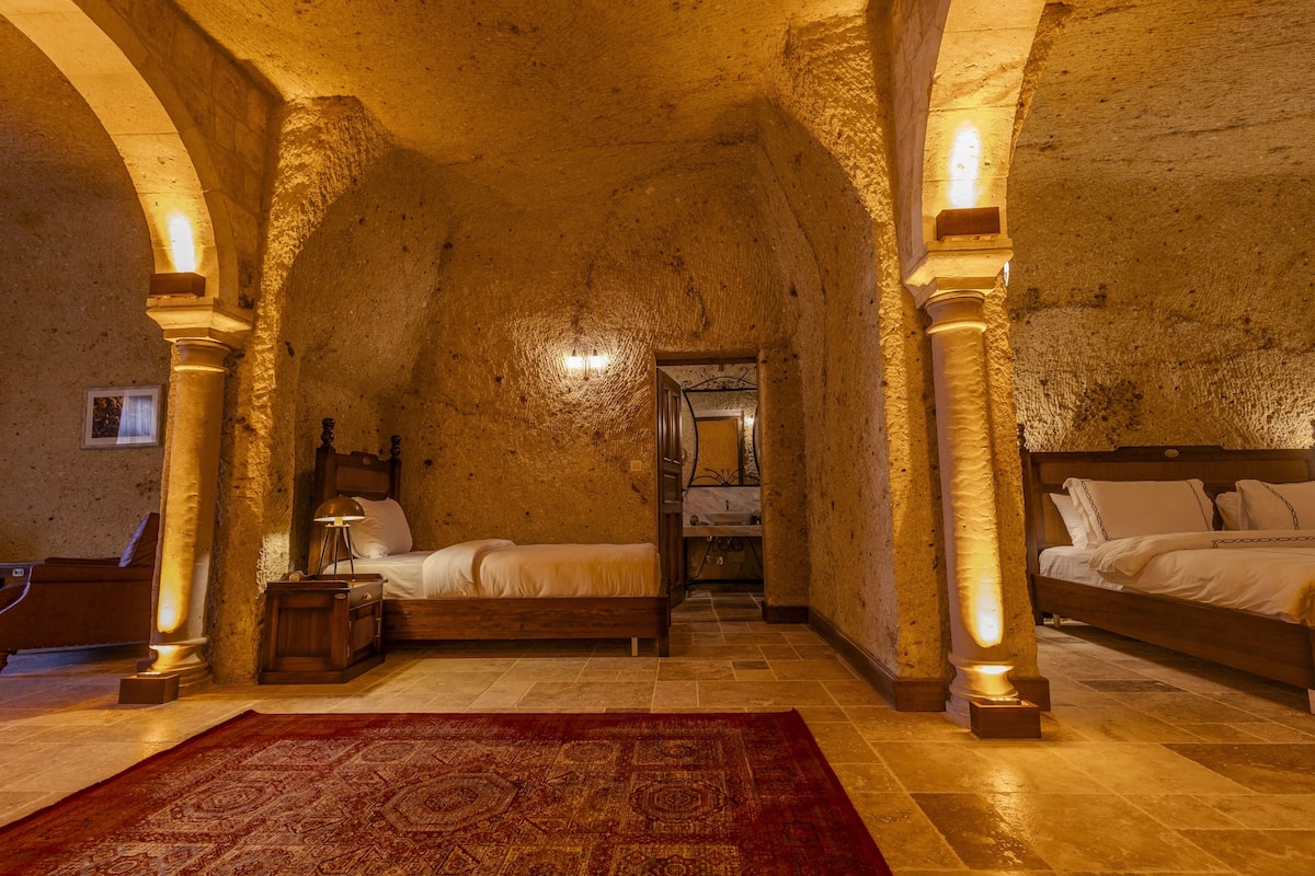 A room with a vaulted ceiling, two beds, a red rug, and stone walls.