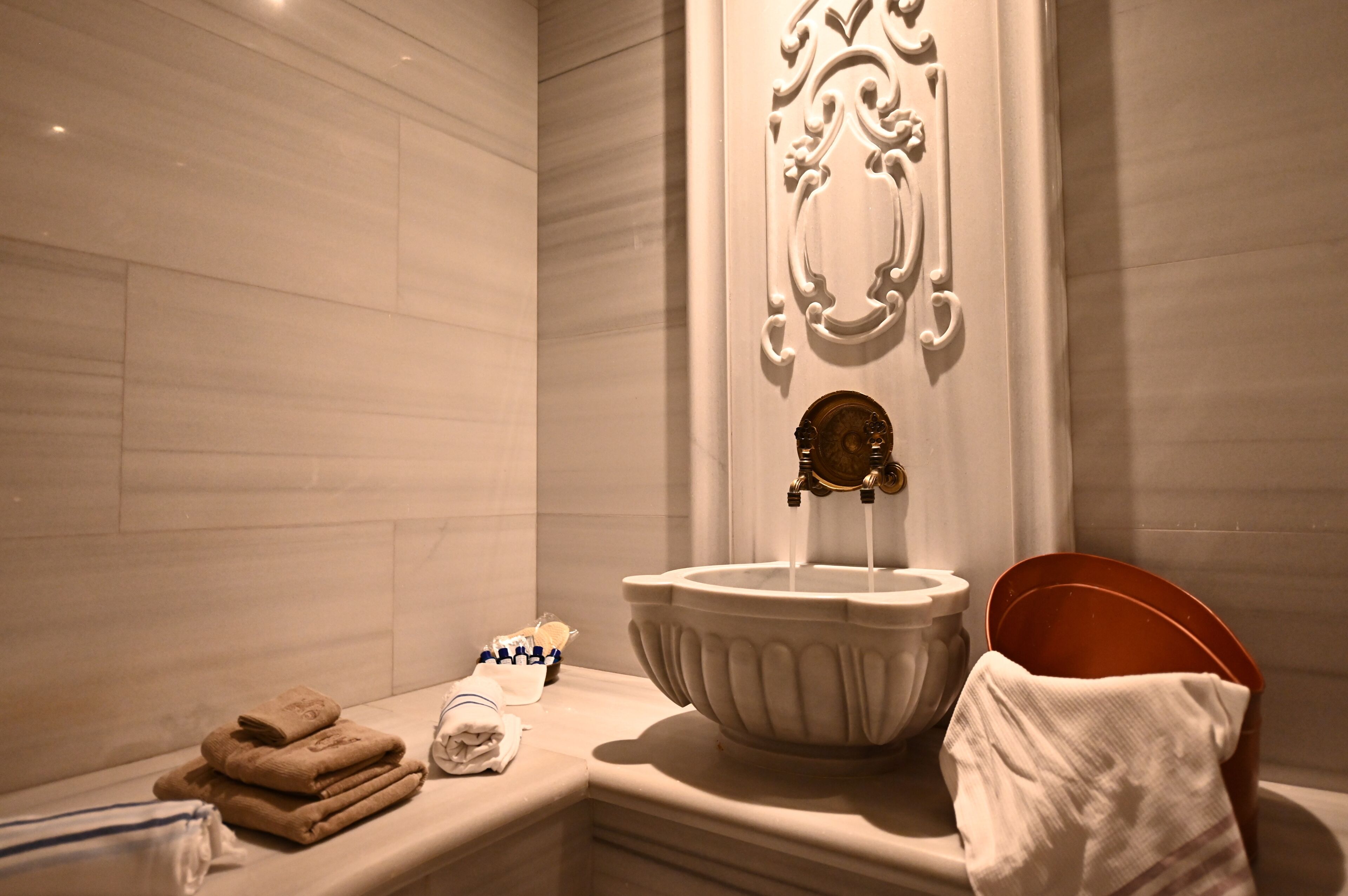 A bathroom with a large sink, a towel rack, and a decorative wall panel.
