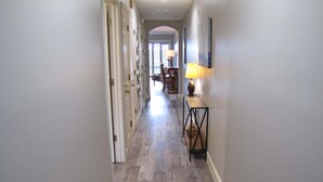 A hallway with wooden flooring, a table with a lamp, and a chair.