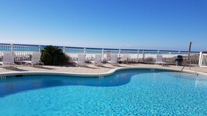 A clear blue swimming pool with a white deck, surrounded by white chairs and a white fence.