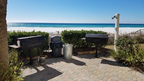 A patio with outdoor grills, a trash can, and a view of the beach.