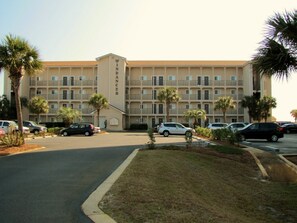 A multi-story hotel with a central entrance, parking lot, and palm trees. - Windancer by Crystal Waters (Destin)