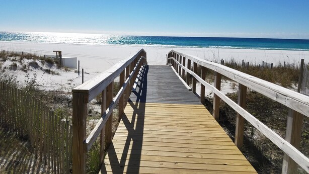 A wooden boardwalk leading to a beach with white sand and clear blue water.