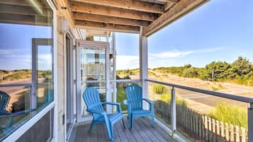A covered outdoor area with two blue Adirondack chairs, a glass door leading to a room, and a view of a road and greenery.