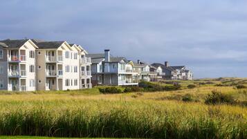 A row of multi-story residential buildings with balconies, situated on a grassy hill with a clear sky above.