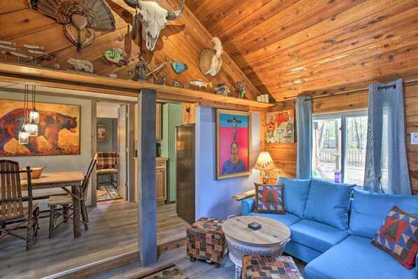A rustic cabin interior with a dining area, a blue sofa, and a kitchen visible through an open door.