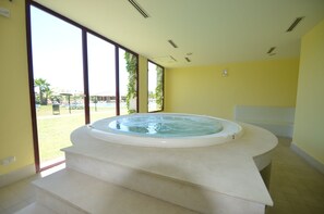 A room with a hot tub, large windows, and a view of the outdoors.