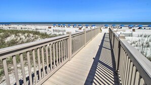 A wooden boardwalk leading to a beach with blue umbrellas and lounge chairs. - Lagoon & Fountain Views: Villa in Palmetto Dunes (Hilton Head)