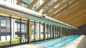 An indoor swimming pool with a long, narrow design, surrounded by large windows and a wooden ceiling structure. - Penthouse Apartment in Melb CBD Perfect Location (Melbourne)