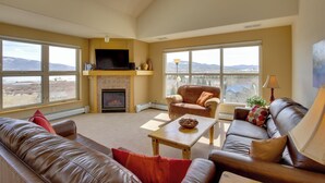 A spacious living room with a fireplace, leather sofas, a television, and large windows offering a mountain view. - 360 Mtn Views & Shared Hot Tub: Cozy Frisco Condo! (Frisco)