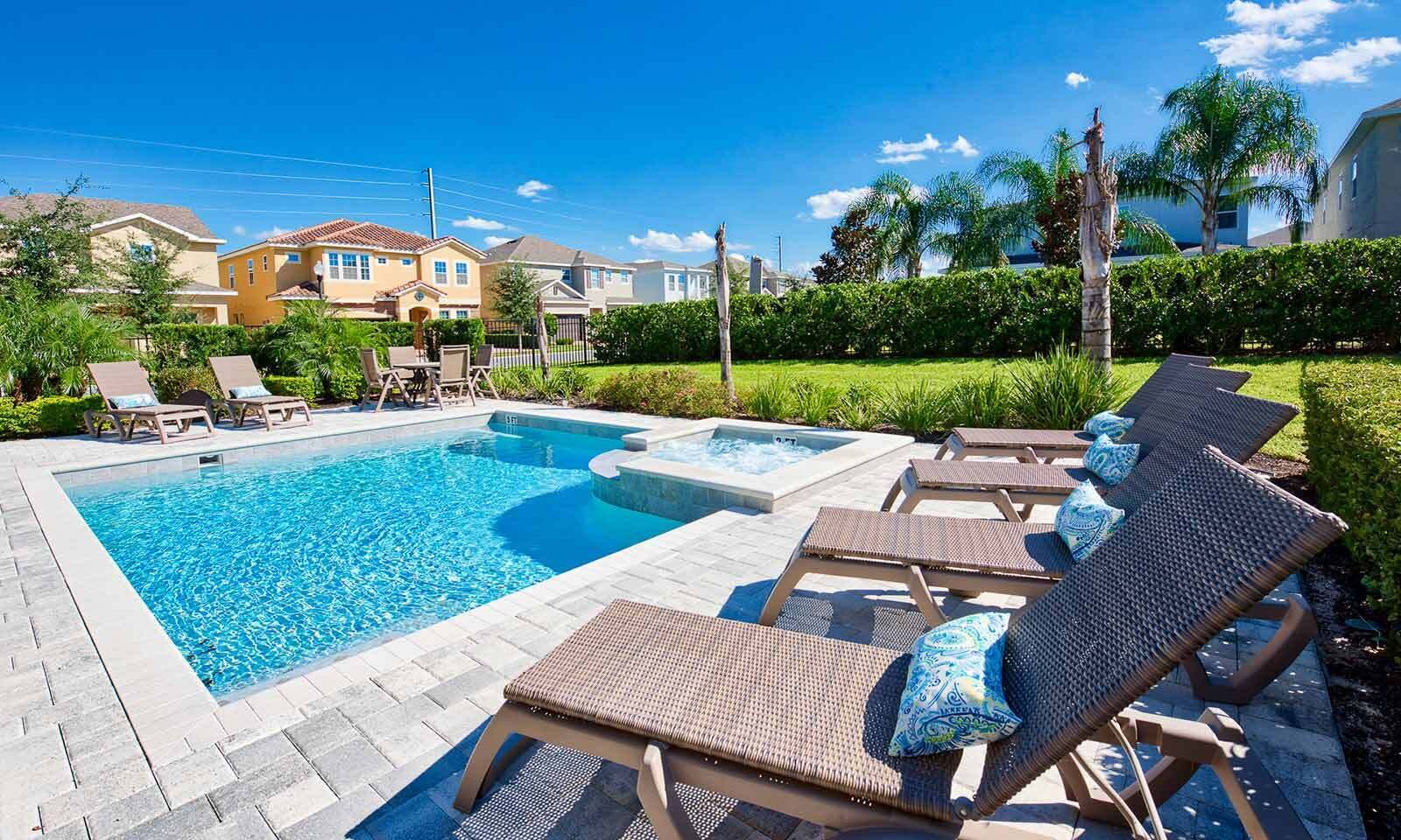 A rectangular swimming pool with lounge chairs and a hot tub, surrounded by a landscaped garden and residential buildings.