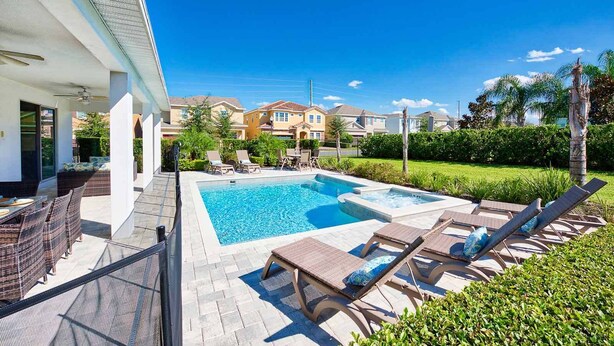 Une piscine avec des chaises longues, un patio aménagé avec des meubles en osier et une vue sur les maisons voisines.