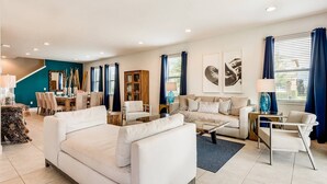 Un salon spacieux avec un grand canapé blanc, un canapé plus petit, une table basse et un coin repas comprenant une table et des chaises en bois.