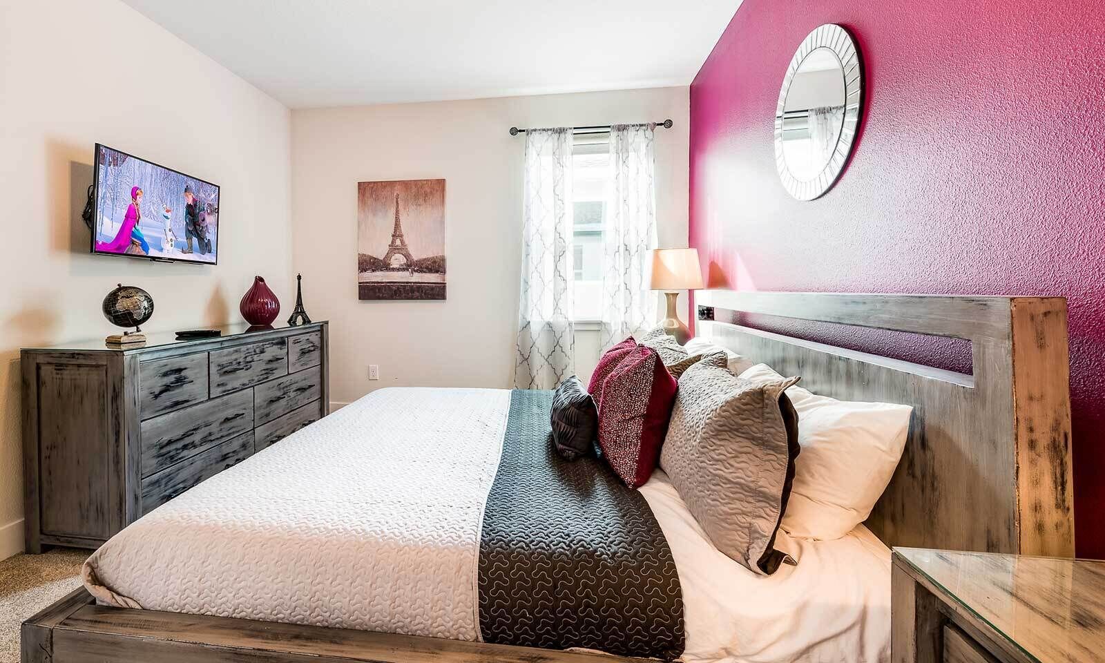 A bedroom with a bed, a dresser, a television, a painting of the Eiffel Tower, and a mirror on the wall.