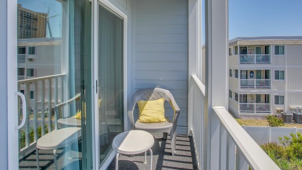 A balcony with two white chairs, one with a yellow cushion, and a small table. - Walk to Ocean: Myrtle Beach Condo w/ Screened Deck (Myrtle Beach)
