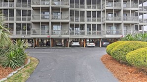 A multi-story hotel with balconies, a parking area, and a well-maintained garden. - Walk to Ocean: Myrtle Beach Condo w/ Screened Deck (Myrtle Beach)