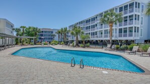 A swimming pool with lounge chairs and palm trees, surrounded by a multi-story building with balconies. - Walk to Ocean: Myrtle Beach Condo w/ Screened Deck (Myrtle Beach)