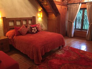 Ein gemütliches Schlafzimmer mit einem Holzkopfende, einer roten Bettdecke und einem passenden roten Teppich.