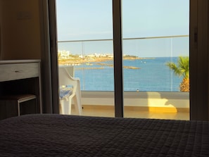 A room with a bed, a chair, and a large window overlooking a body of water and a distant shoreline.