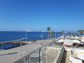 A seaside terrace with outdoor seating, a view of the ocean, and palm trees.