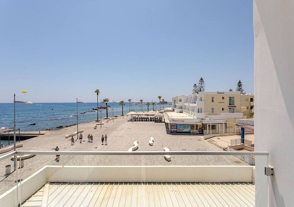 A beachside view from a balcony with a clear sky, a sandy beach, and a few people.
